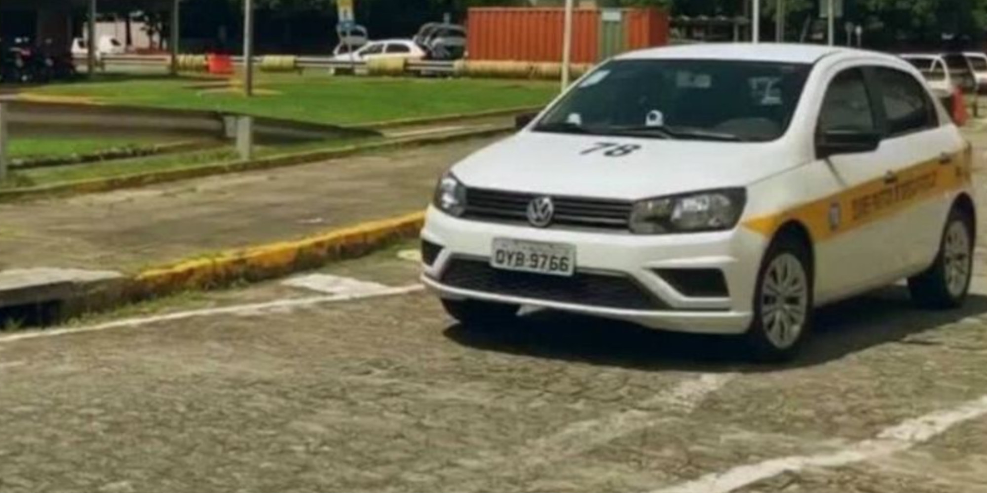 Carro branco passando numa via do trecho da pista para a prova prática de habilitação