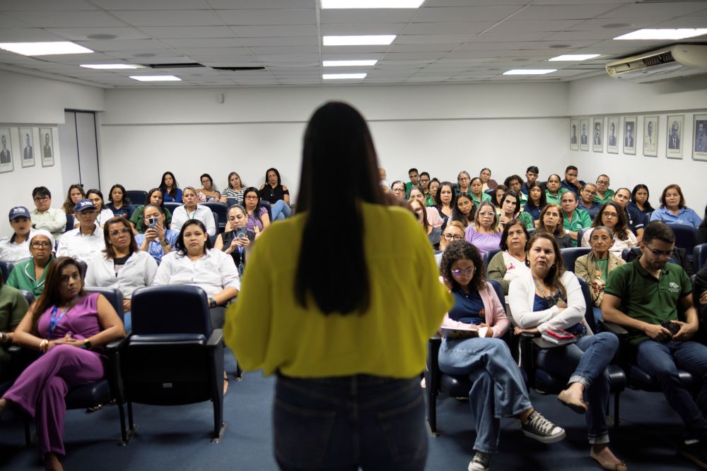 Mulher de frente para a plateia vestindo blusa amarela