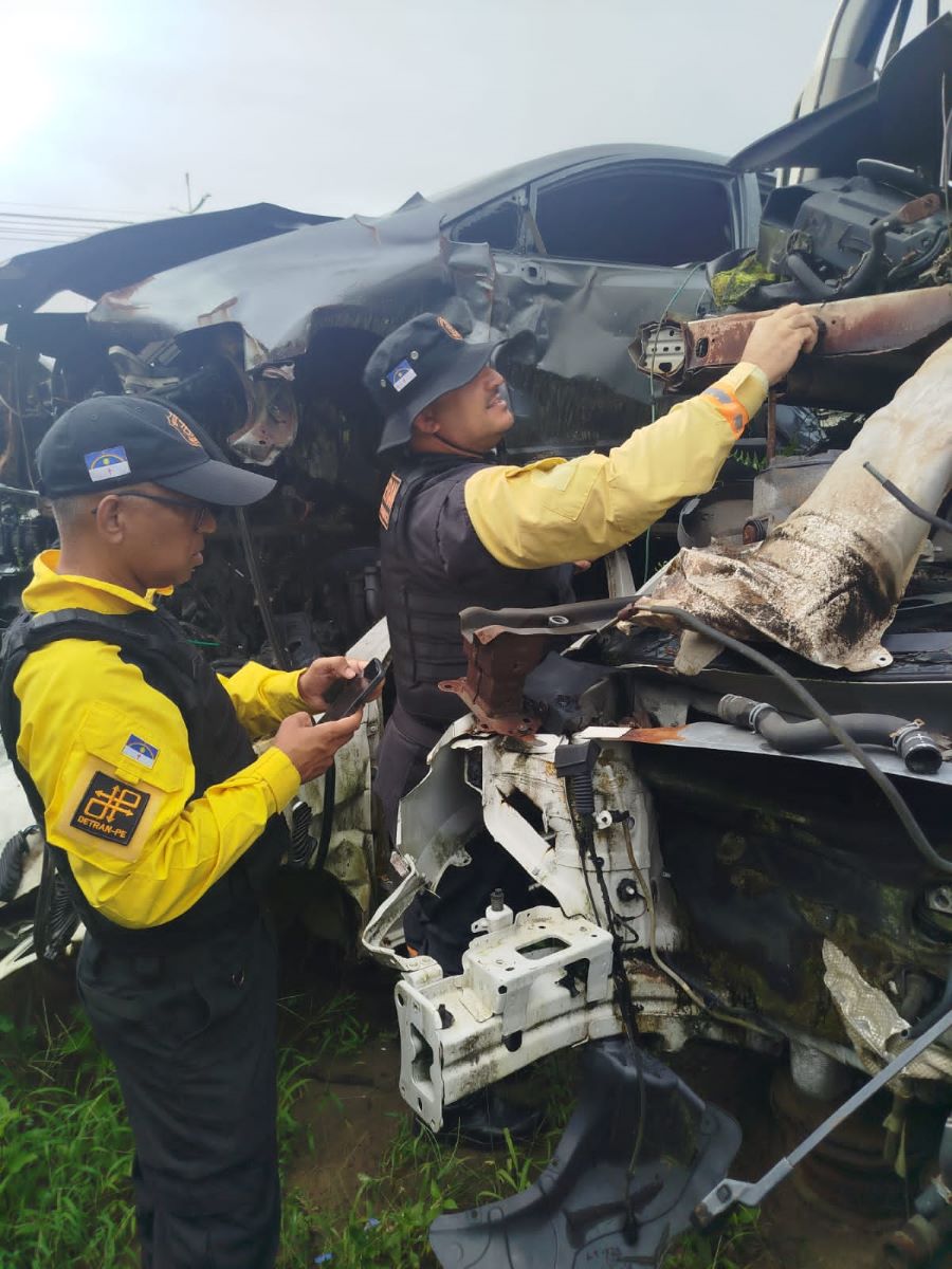 02 agentes de trânsito do DETRAN-PE analisando peças de carros usados no depósito.