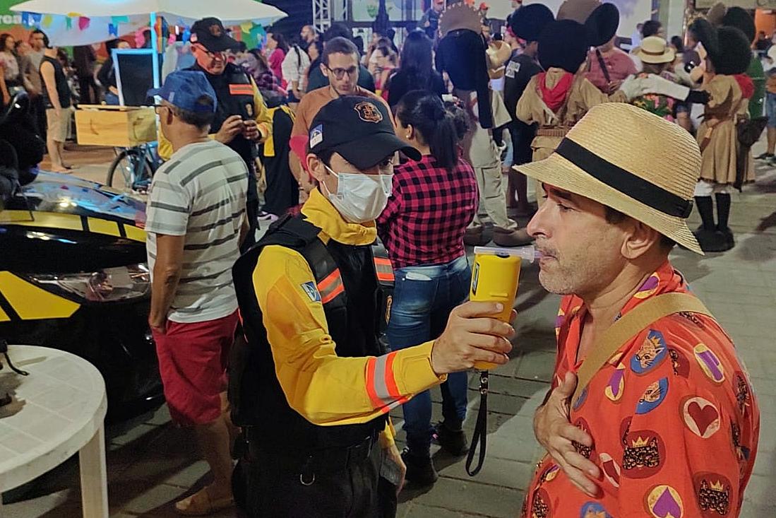 Fotografia colorida de agente de trânsito realizando teste do bafômetro em popular