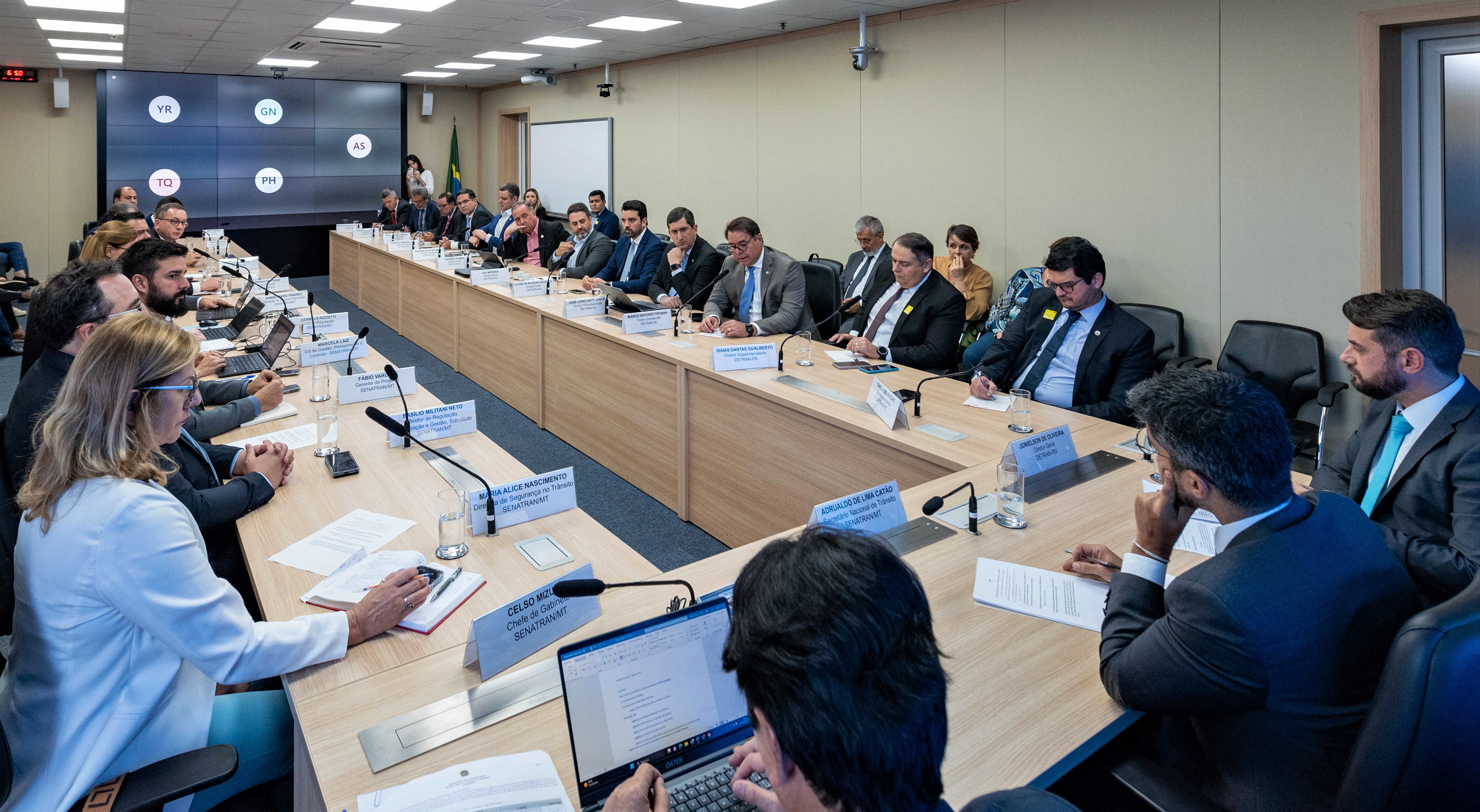 Fotografia colorida mostrando mesa de reunião com formato em U ocupada por integrantes do encontro