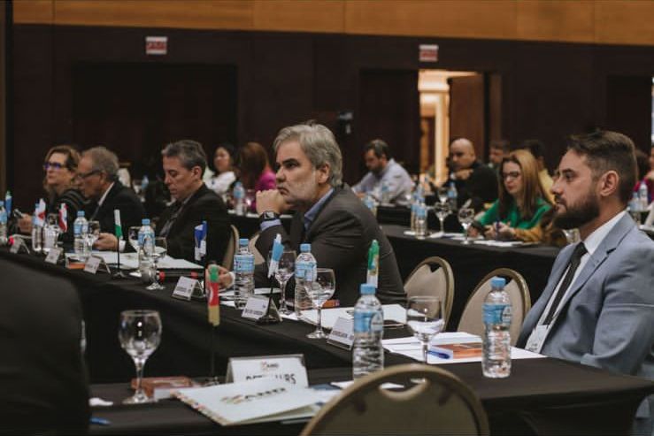Na foto, o Diretor Presidente do DETRAN-PE, Gustavo Carneiro Leão, de perfil, com a mão esquerda no queixo e com teu cotovelo encostado na mesa. Na foto, ele está ao centro da imagem, sentado na cadeira, ao seu redor, outros Diretores Presidente dos DETRAN’s do Brasil. Essa imagem é do 74º Encontro Nacional dos Detrans, que aconteceu em Florianópolis (SC).