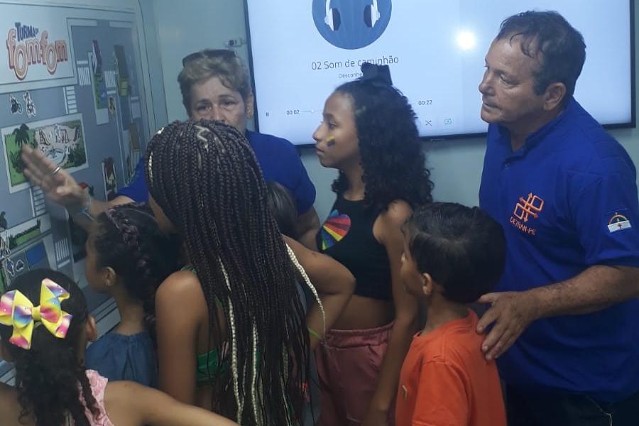 Na foto, dois educadores de trânsito, uma mulher e um homem, estão mostrando para as crianças atividade educativa sobre respeito no trânsito.