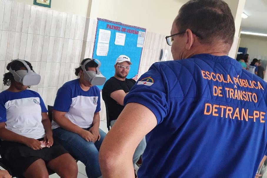 Na foto, educador de trânsito do DETRAN-PE e duas alunas utilizando os óculos de realizada virtual.  