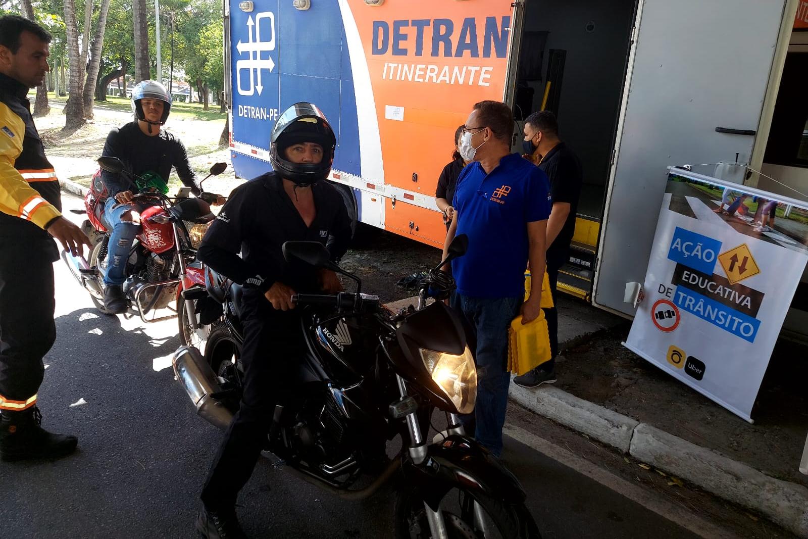 Na foto, agente de trânsito e educador de trânsito do DETRAN-PE realizando abordagem em motociclista na ação educativa. Ao fundo, o Caminhão do DETRAN Itinerante.