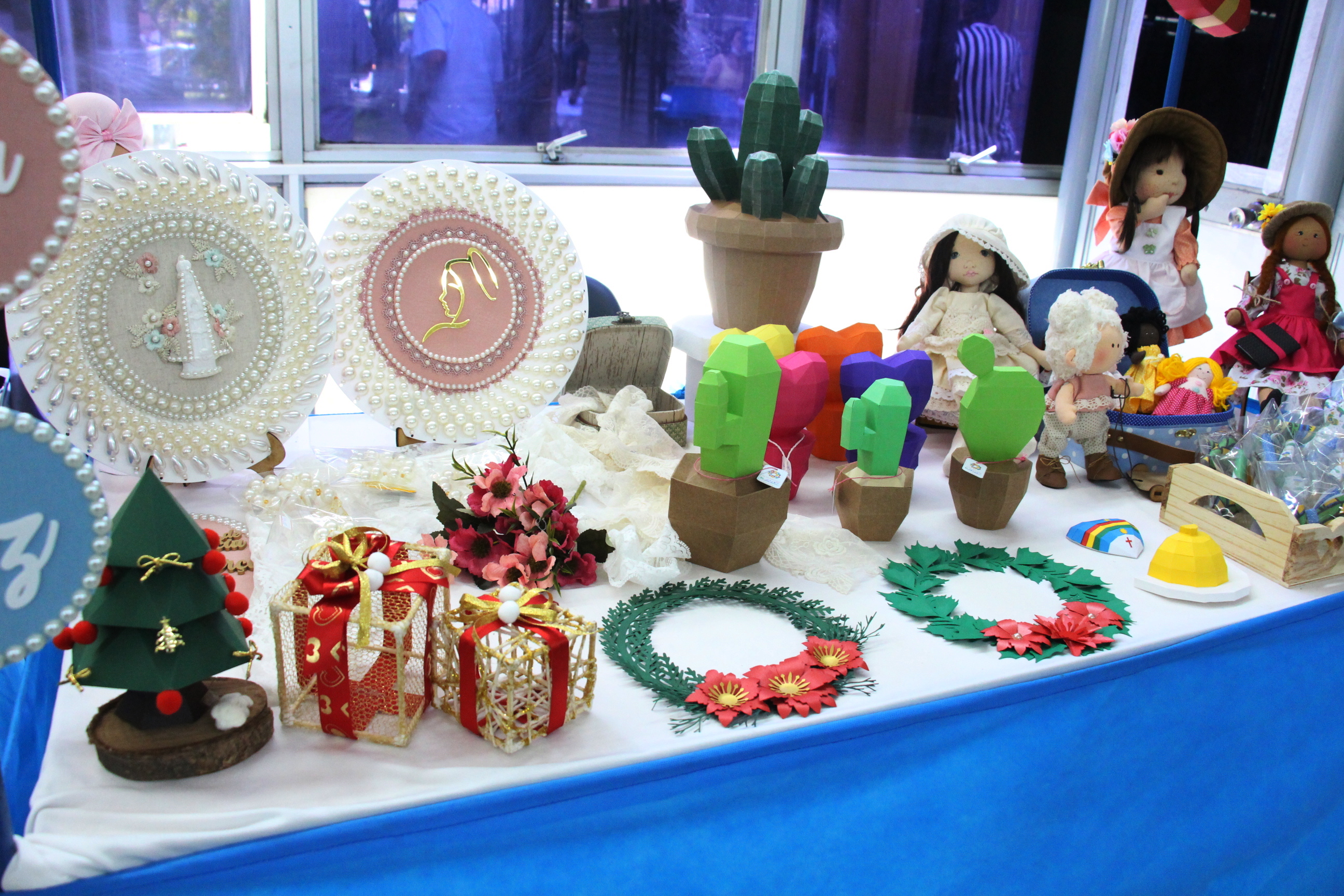 Detalhe de fotografia colorida com produtos de um estande mostrando bonecas de pano, artigos em madeira e tecido