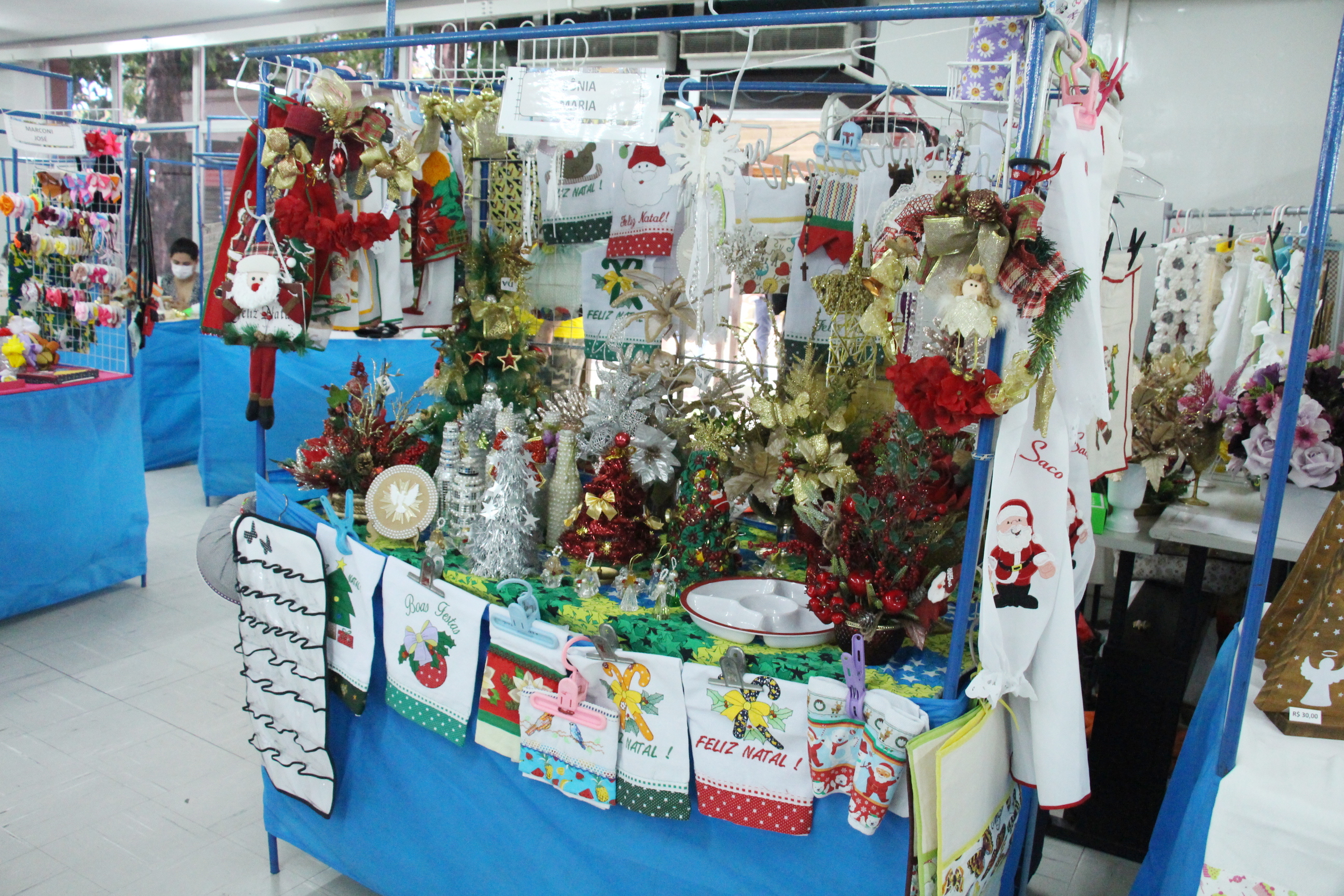 Foto colorida mostra três moças comprando produtos de um estande a uma das artesãs