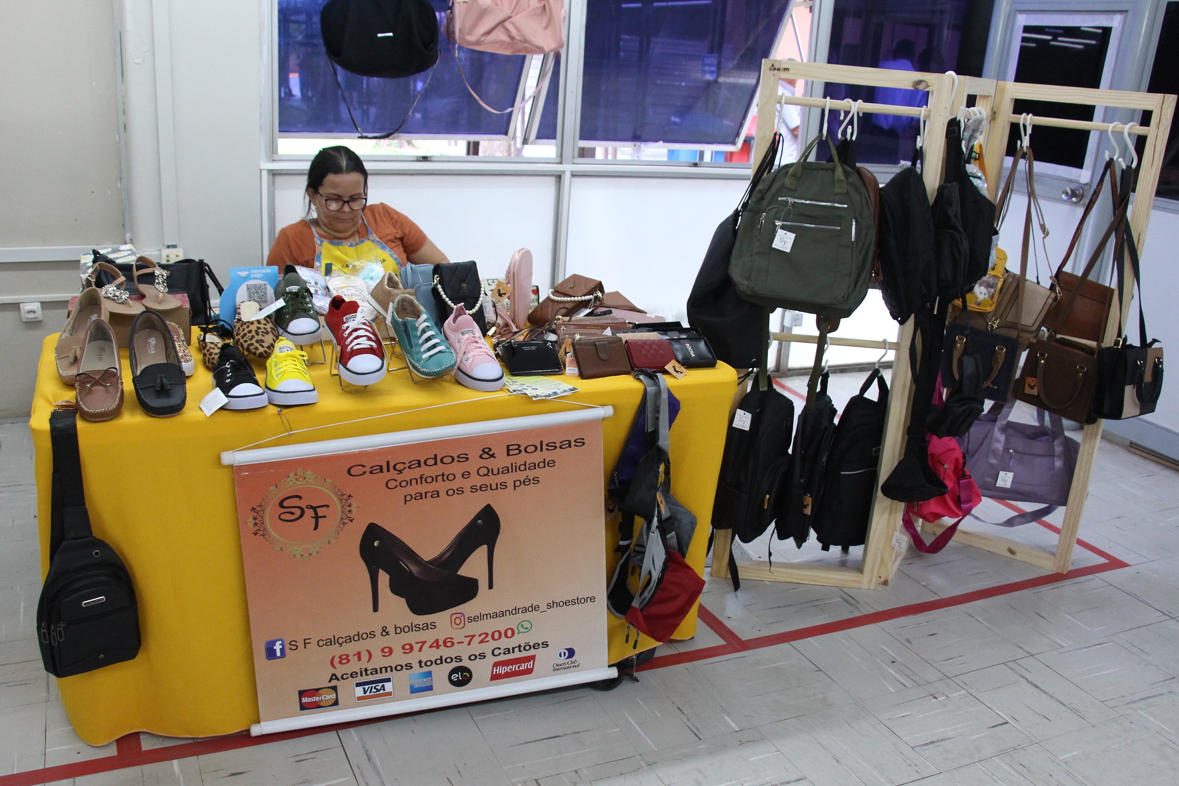Na foto, uma barraca com exposição de sapatos e carteiras. Ao lado, expositor de bolsas.