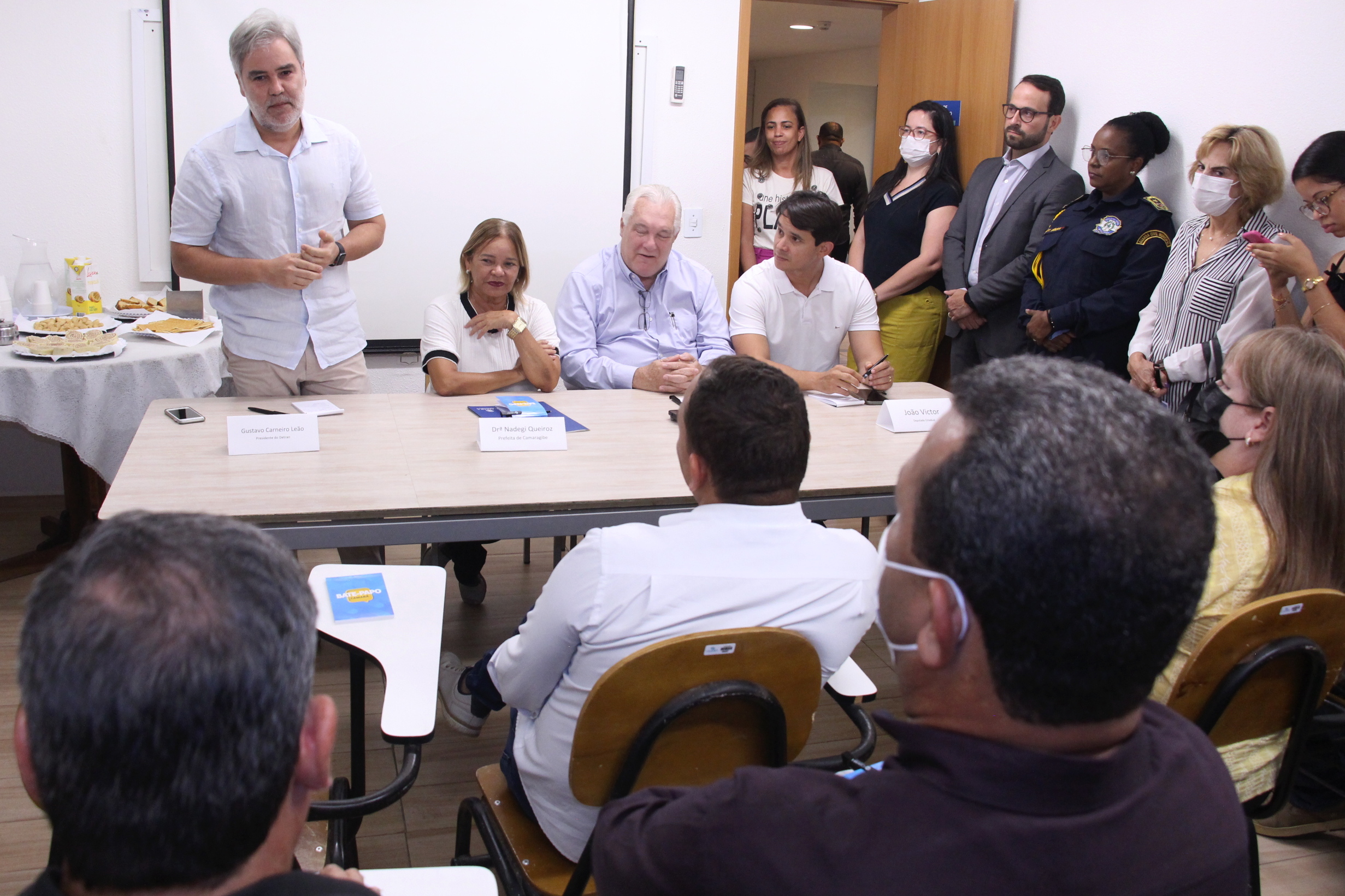 Na foto, o Diretor Presidente do DETRAN-PE, Gustavo Carneiro Leão, em pé, discursando para funcionários do shopping camará, representantes da prefeitura e do governo do Estado, em encontro sobre a implantação da loja da Autarquia naquele centro comercial. Ao seu lado, a Prefeita de Camaragibe, Nadegi Queiroz; o Empreendedor do Shopping Camará, Jorge Corte Real; e o Deputado Estadual eleito, João Victor. 