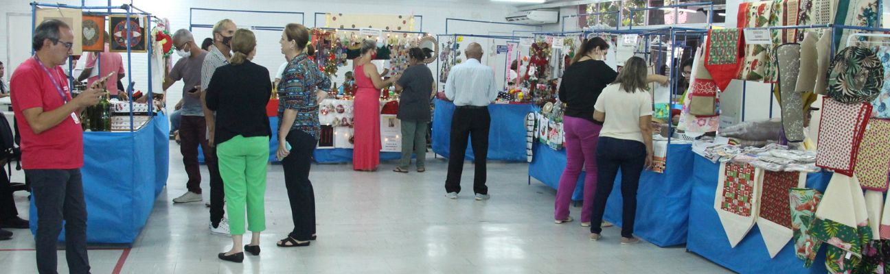 Fotografia colorida do salão de entrada do Detran-PE mostrando pessoas visitando as barraquinhas da feira