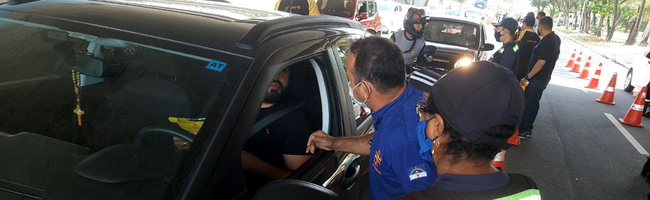 Na foto, educador de trânsito do DETRAN-PE e agente do DER abordando motorista em ação educativa. Ao fundo, agente de trânsito do DETRAN-PE e um outro carro sendo abordado na ação educativa. 
