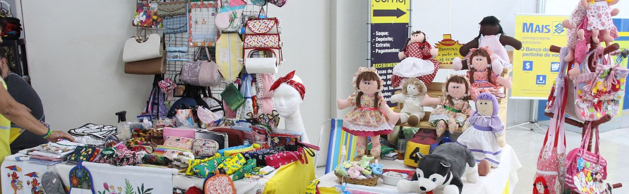 Na foto, duas barracas com exposição de bonecas de pano, bolsas, pelúcias e artes manuais.
