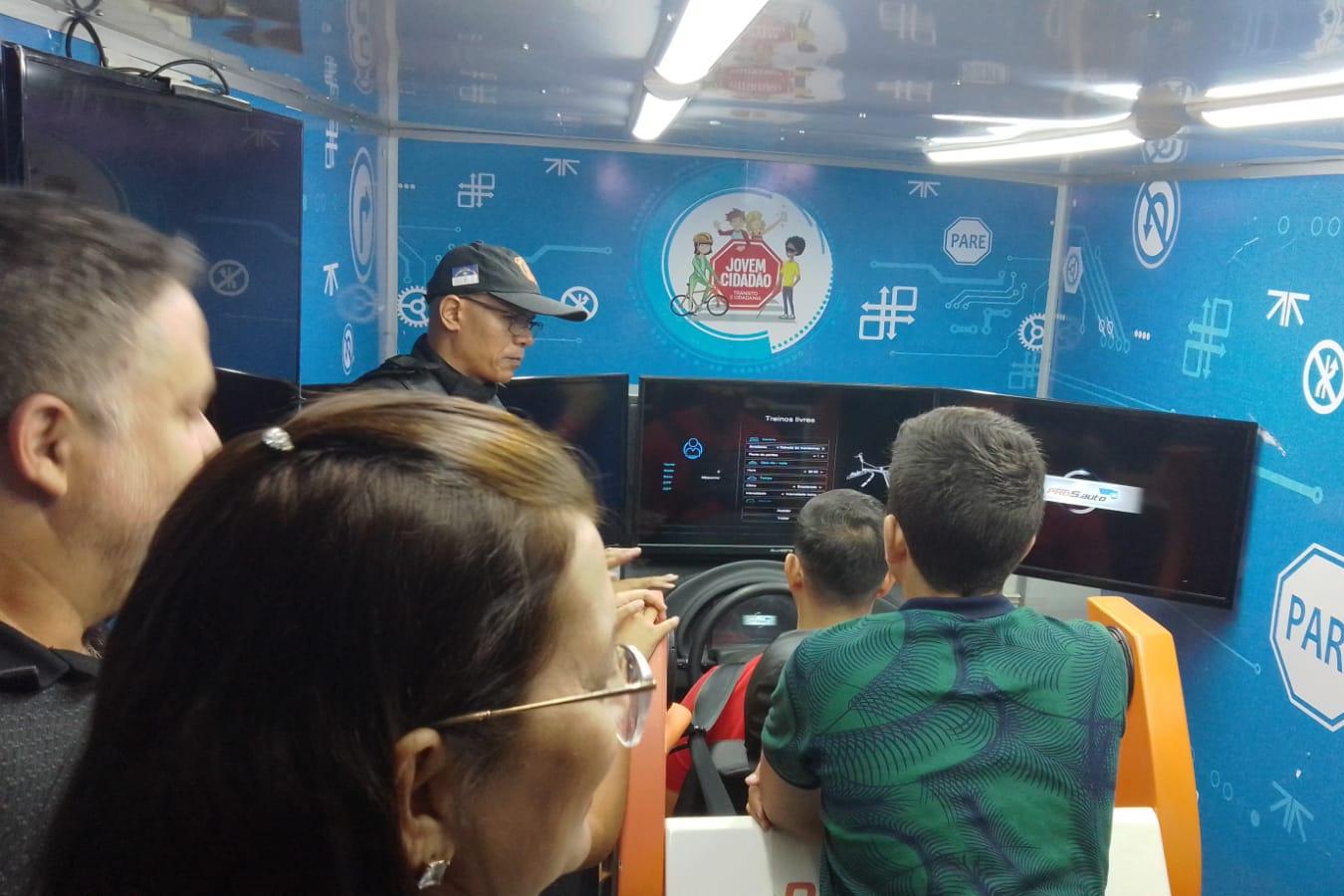 Jovens utilizando simulador com ajuda do agente do Detran