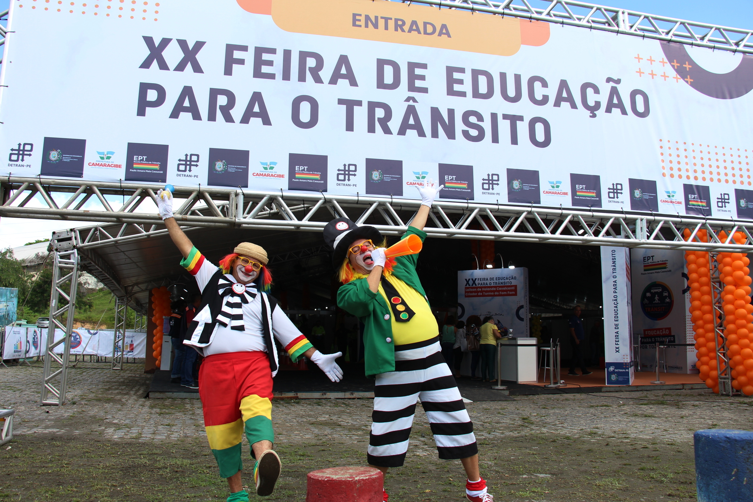 Na foto, dois arte educadores do DETRAN-PE, vestidos da Turma do Fom-Fom, respectivamente, Fom-Fom e Tio Buzina, pousando na entrada da 20º Feira de Educação para o Trânsito de Pernambuco, instalada na Praça de Eventos de Camaragibe.