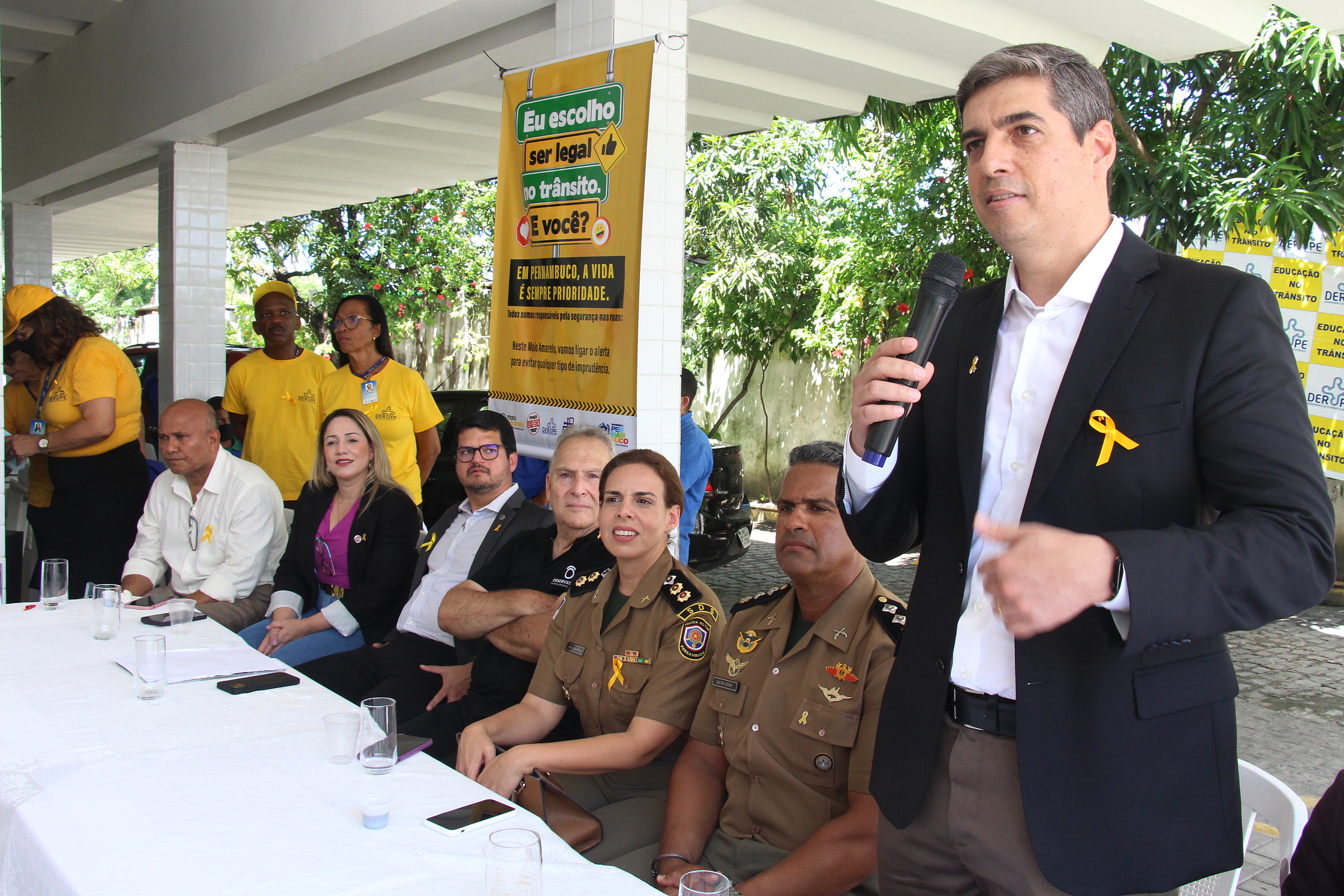 Na foto, o Diretor Presidente do DER, Rivaldo Rodrigues de Melo Filho, realizando sua fala na abertura do Movimento Maio Amarelo na sede do DER. Ele está em pé e ao seu lado, autoridades de trânsito de todo o Estado de Pernambuco.