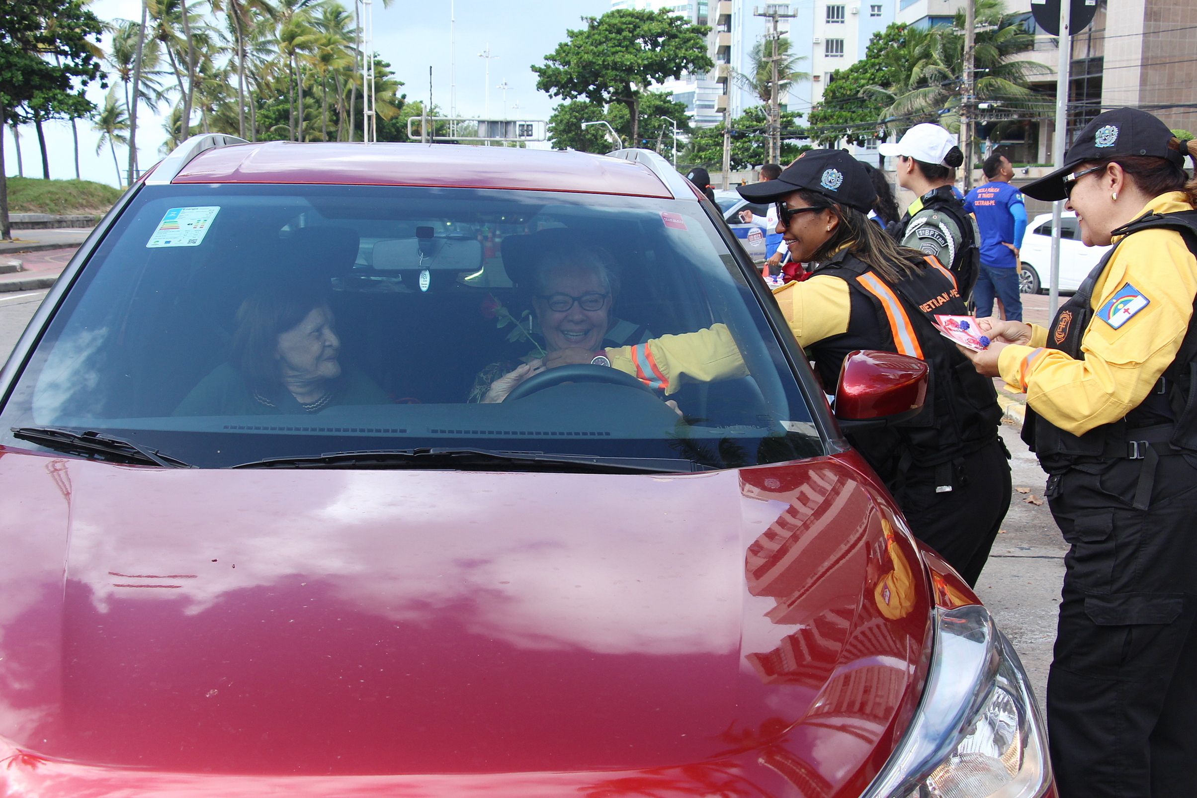 Na foto, agentes de trânsito femininas do DETRAN-PE entregando rosas para motoristas mulher na ação em homenagem ao dia das mulheres.