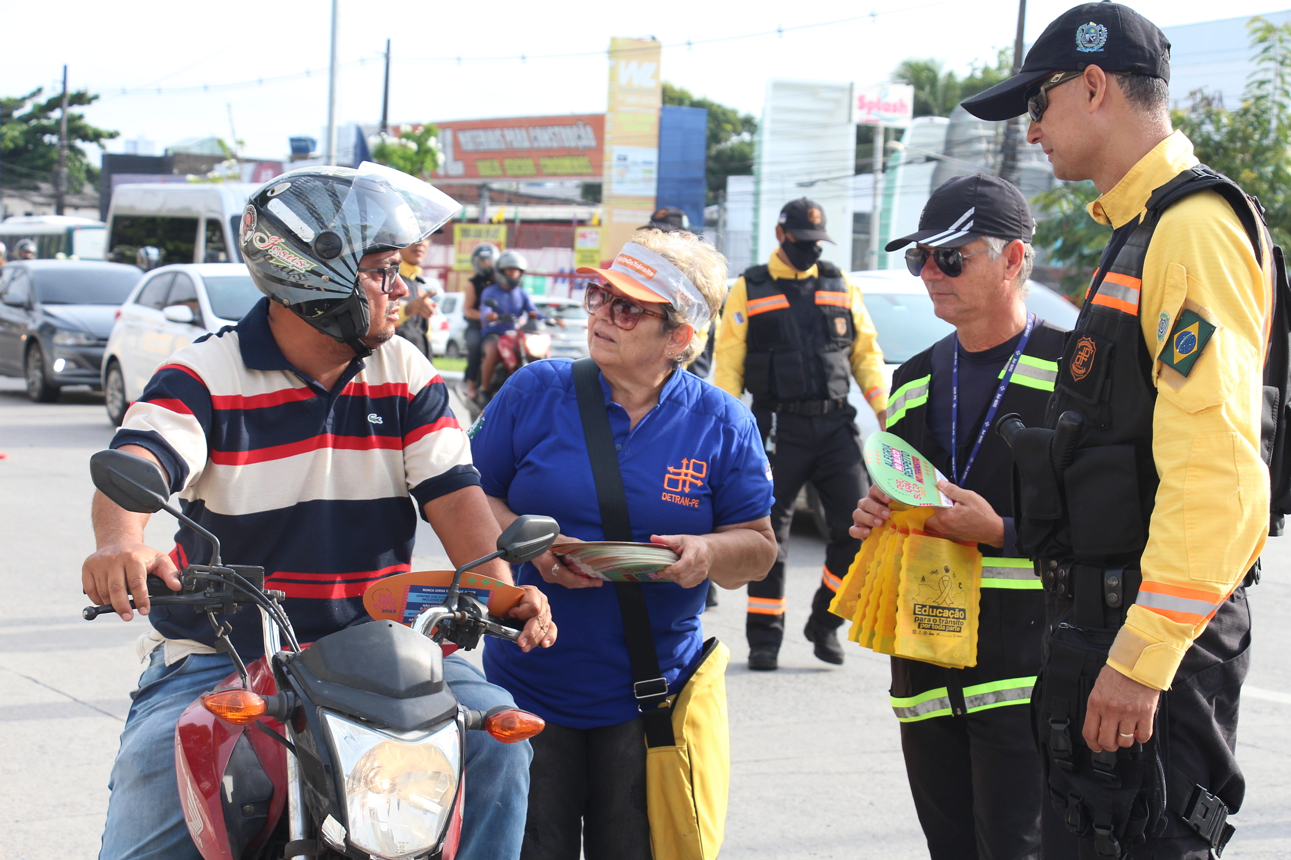 Na foto, um motociclista sendo abordado por educadora de trânsito e agentes de trânsito do DETRAN-PE e DER.
