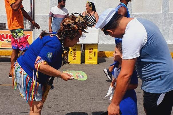 Na foto, educadora de trânsito do DETRAN-PE abordando um pai e seu filho. No local, ela entregou leque com informações educativas do DETRAN-PE. 