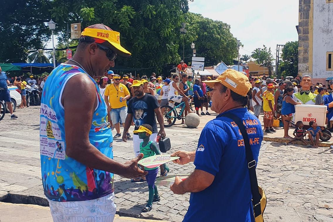 Na foto, educador de trânsito abordando folião em Olinda. Na ocasião, ele recebeu um leque educativo. 