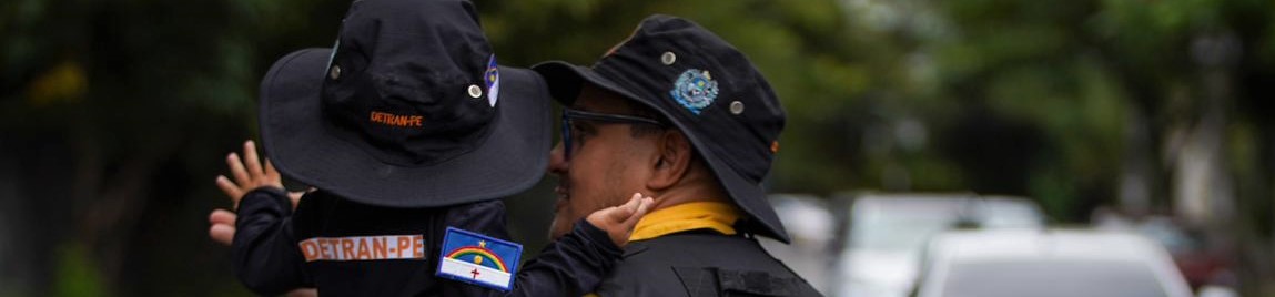 Foto colorida com agente de trânsito e criança no braço