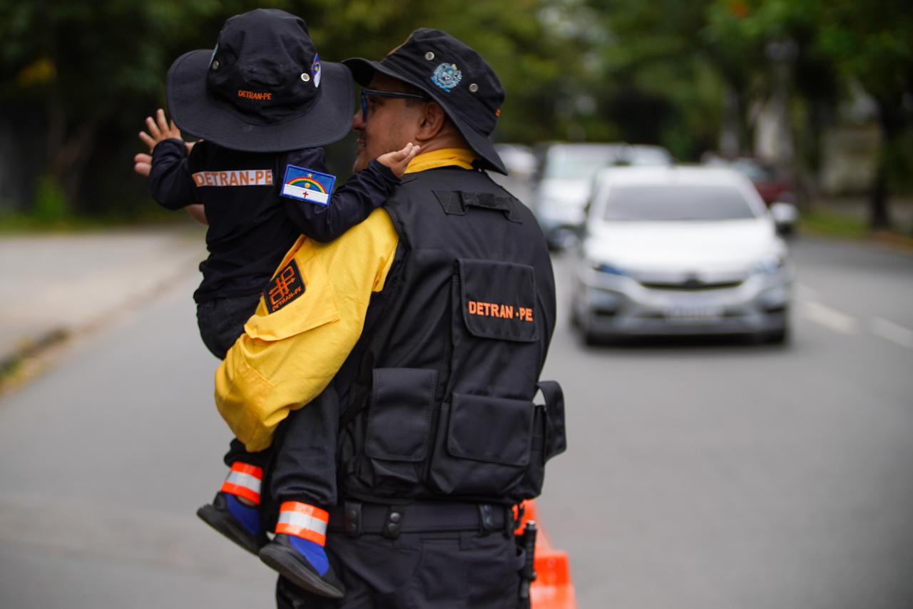 Foto colorida com agente de trânsito e criança no braço