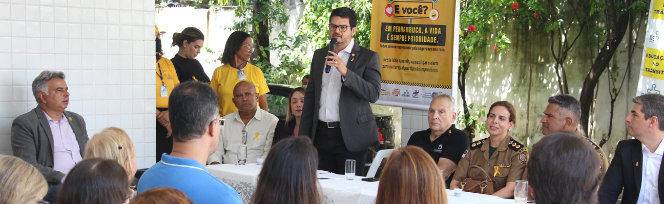 Na foto, o Diretor Presidente do DETRAN-PE, Carlos Fernando Ferreira, realizando sua fala na abertura do Movimento Maio Amarelo na sede do DER. Ele está em pé e ao seu lado, autoridades de trânsito de todo o Estado de Pernambuco.