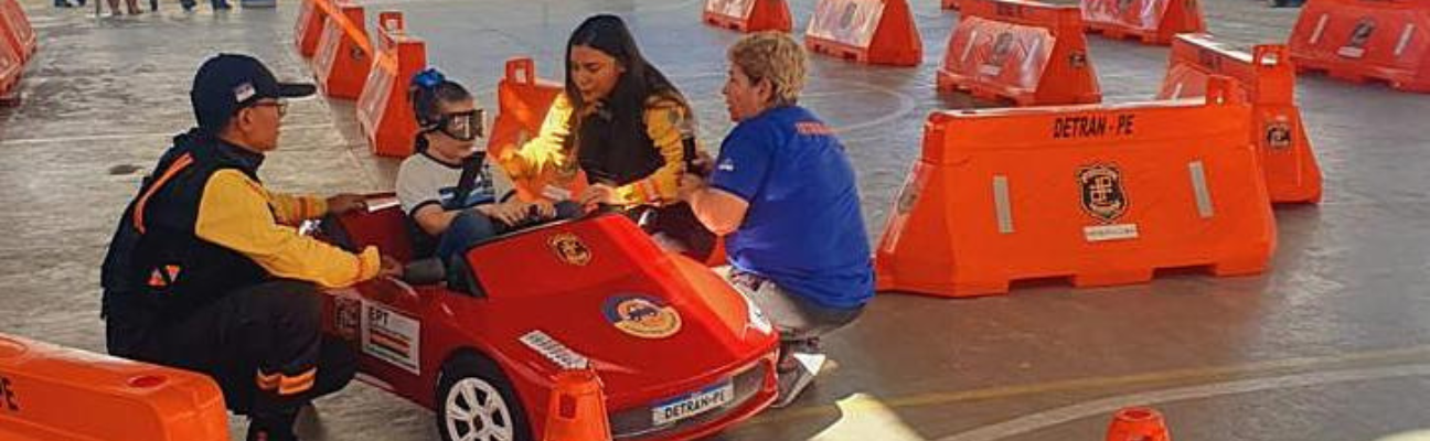 Na foto, educadora de trânsito da Superintendência de Educação de Trânsito, Imprensa e Publicidade Institucional e agentes de trânsito da Diretoria de Fiscalização de Trânsito do DETRAN-PE realizando ação de circuito com carrinhos elétricos, orientando como deve ser o comportamento correto do motorista nas ruas e avenidas, com crianças de escola pública de Jaboatão dos Guararapes. 