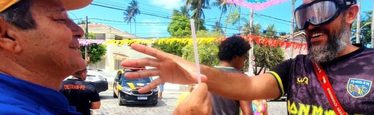 Na foto, educador de trânsito do DETRAN-PE realizando ação educativa com folião. Ele faz o uso do óculos que deixa com a sensação de embriaguez.