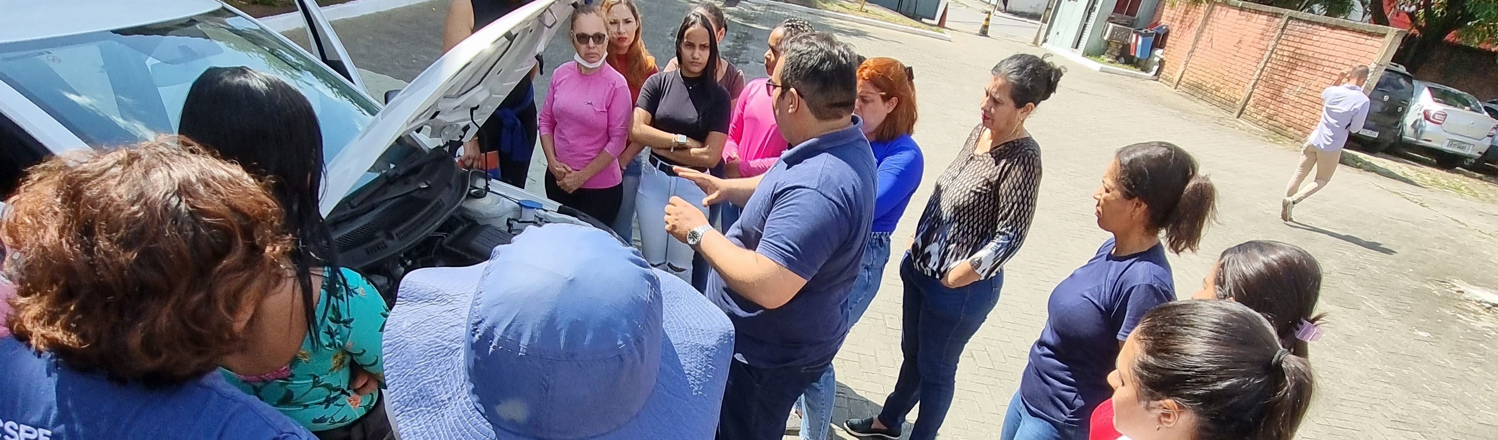 Foto colorida de mulheres em volta de veículo observando motor 