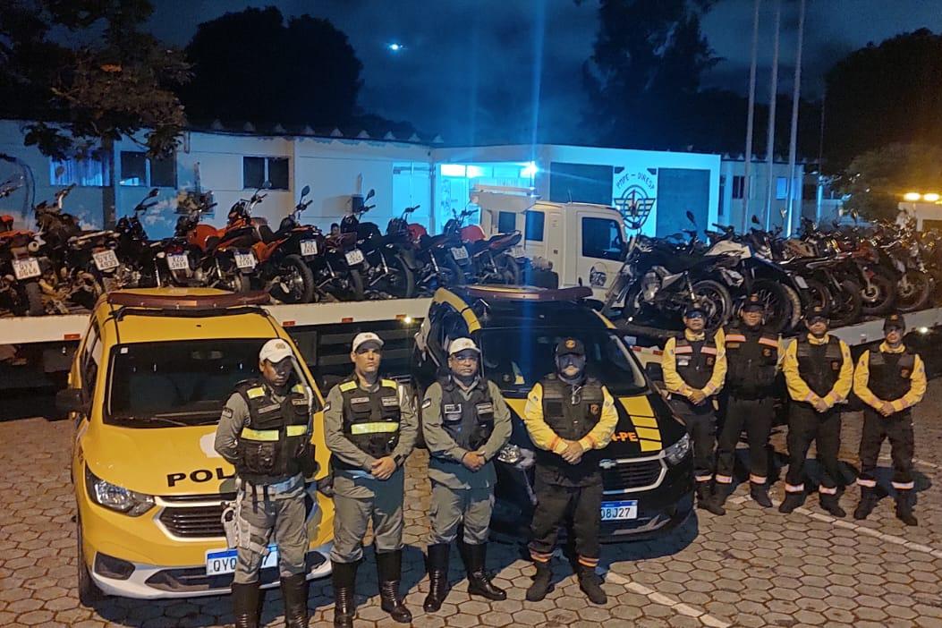 Na foto, em pose de guarda, agentes de trânsito do DETRAN-PE e policiais militares em primeiro plano. Em segundo plano, um veículo da fiscalização de trânsito do DETRAN-PE e uma viatura da PM. Ao fundo, várias motocicletas que foram rebocadas, em cima de um guincho. 