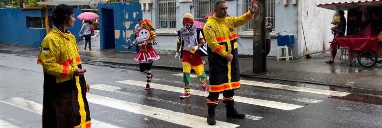 Fotografia colorida mostrando ação em faixa de pedestre com agentes de trânsito e Turma do Fom-Fom