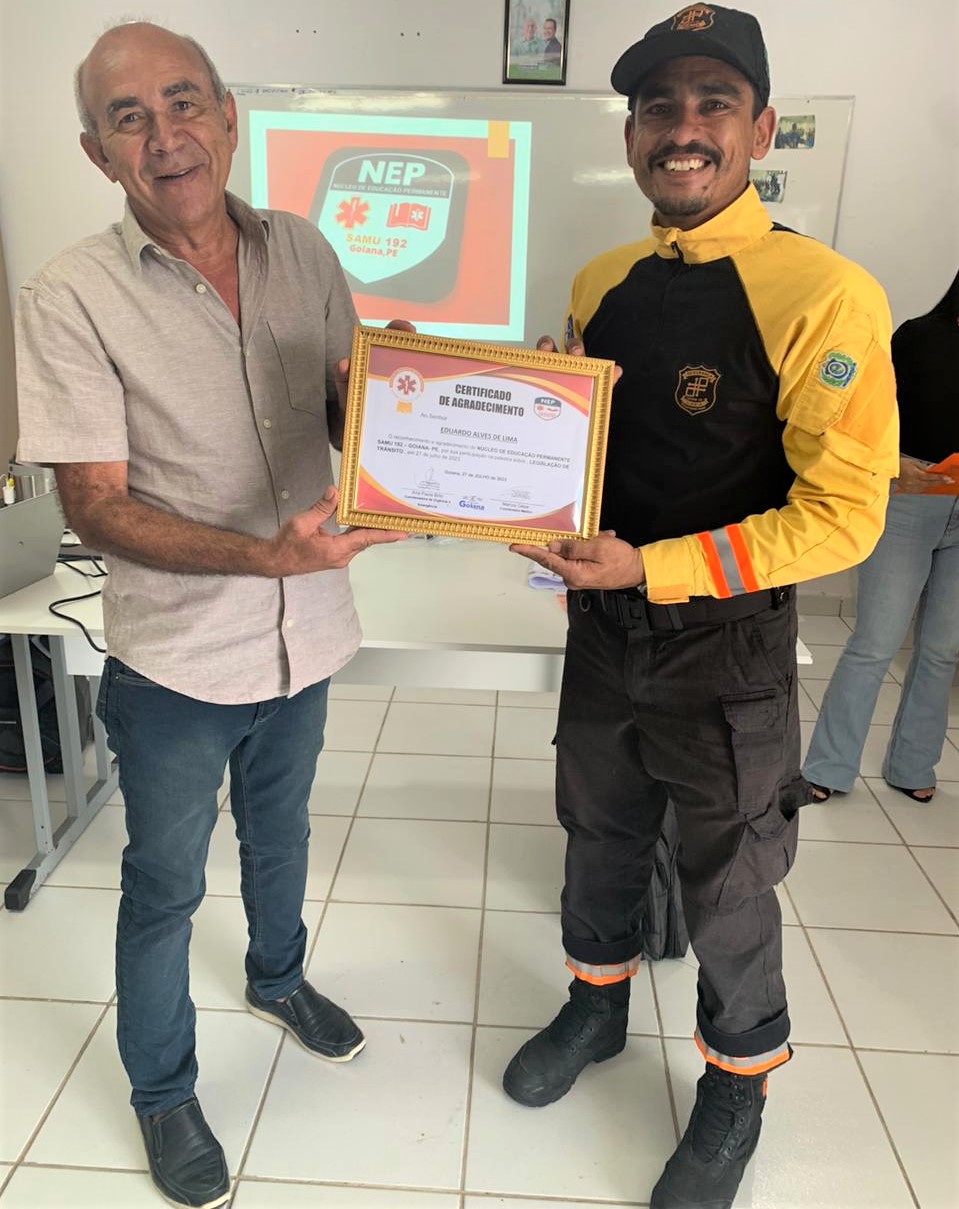 Fotografia colorida mostra agente de trânsito recebendo do prefeito de Goiana certificado de agradecimento  