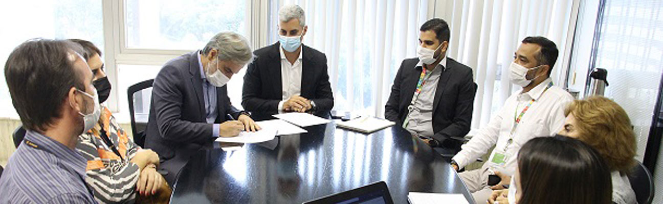 foto de pessoas em reunião ao redor de uma mesa, e o diretor-presidente assinando documento