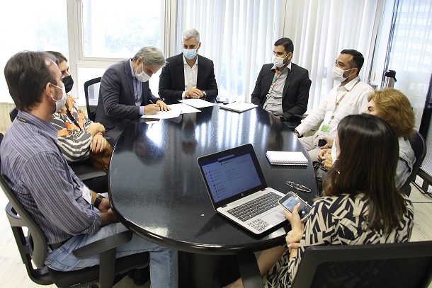 foto de pessoas em reunião ao redor de uma mesa, e o diretor-presidente assinando documento